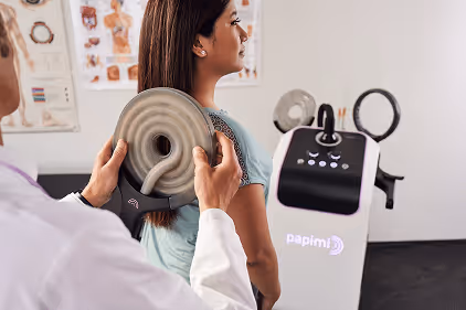 Medical professional holding a coil device near a patient's upper back during a treatment session.